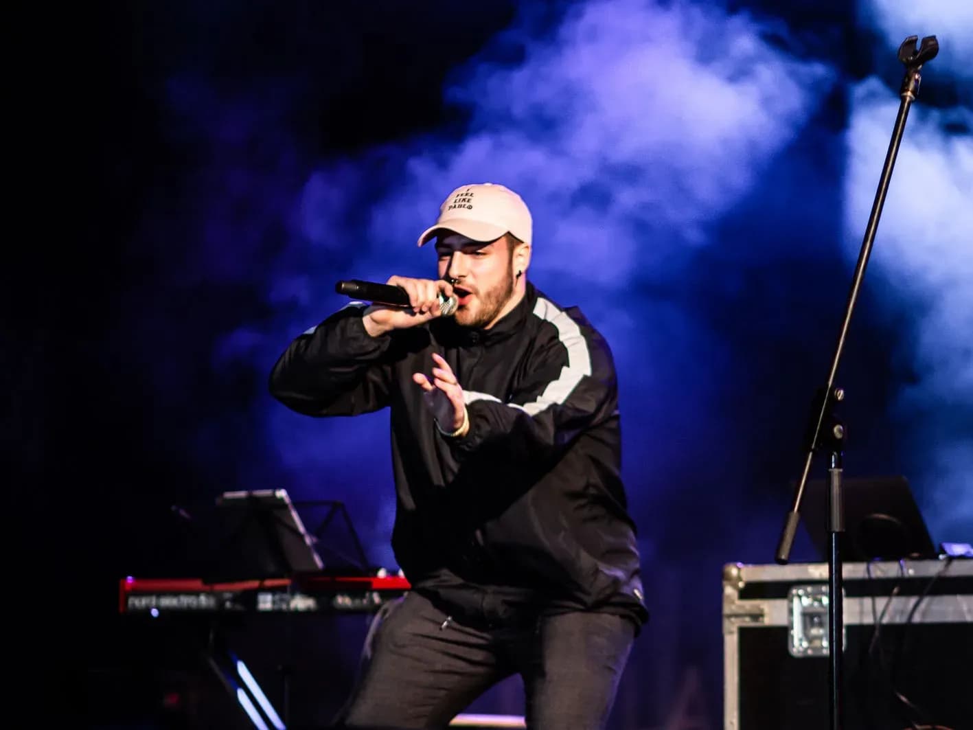AkaEdu rapeando con micrófono en escenario iluminado de azul, sesión en vivo de dembow y trap bailable del MC catalán