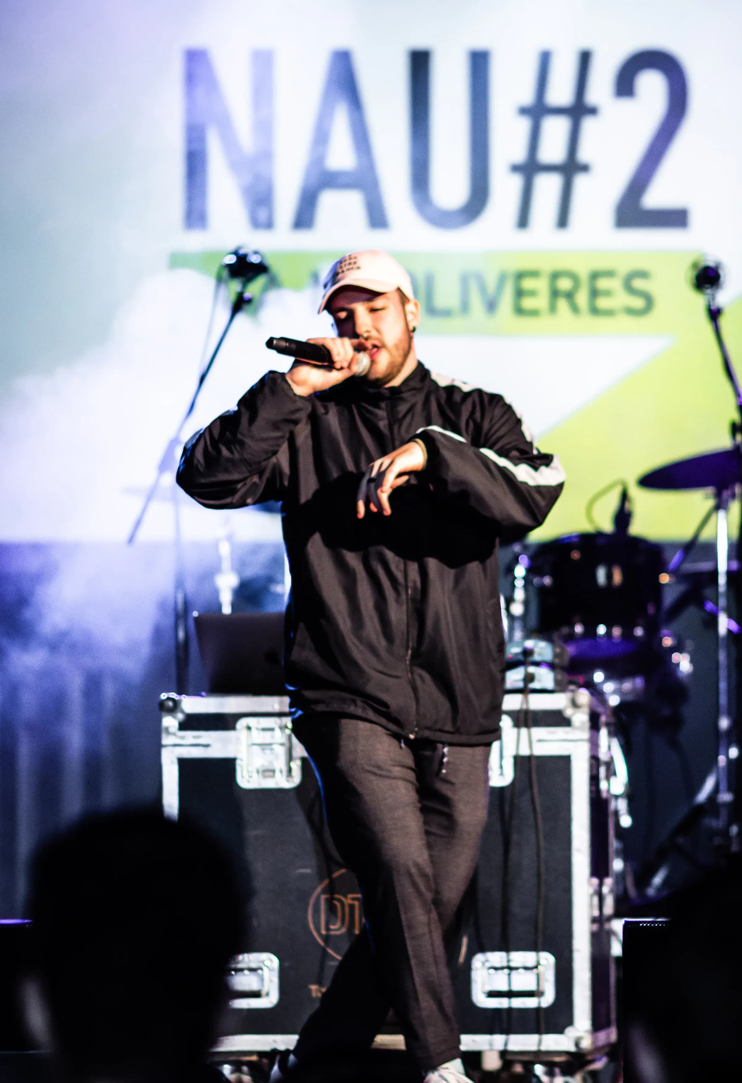 Vocalista con gorra y chandal negro cantando al micro sobre escenario de inauguracion La Nau 2 Oliveres