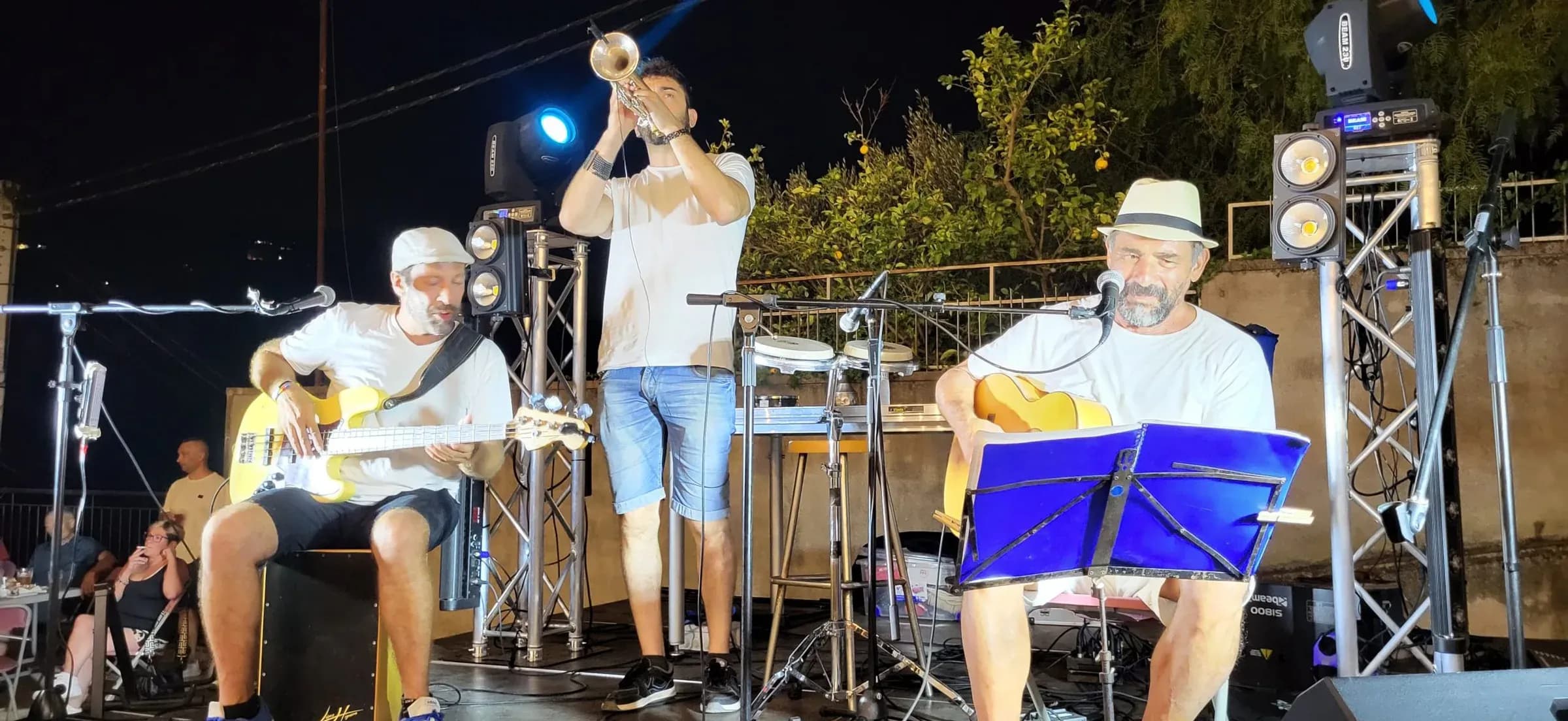 Trío Barreto y Cía tocando en directo al aire libre: guitarra acústica, trompeta y voz en concierto nocturno de versiones