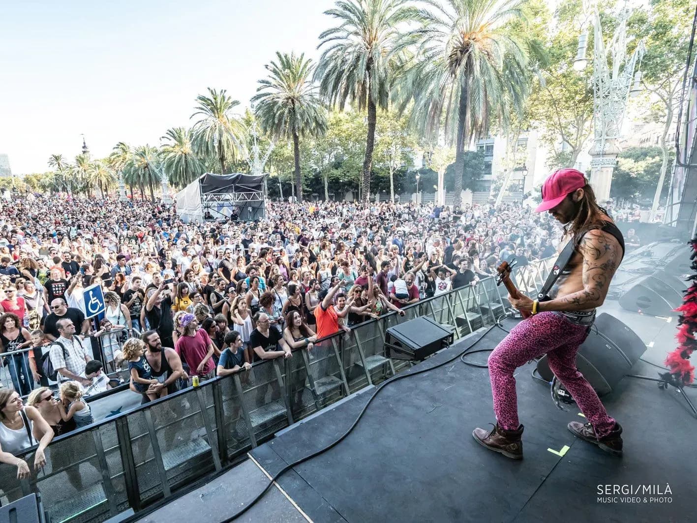 Vocalista de Big Mouthers con gorra roja y pantalón estampado animando a multitud bajo palmeras en concierto de versiones