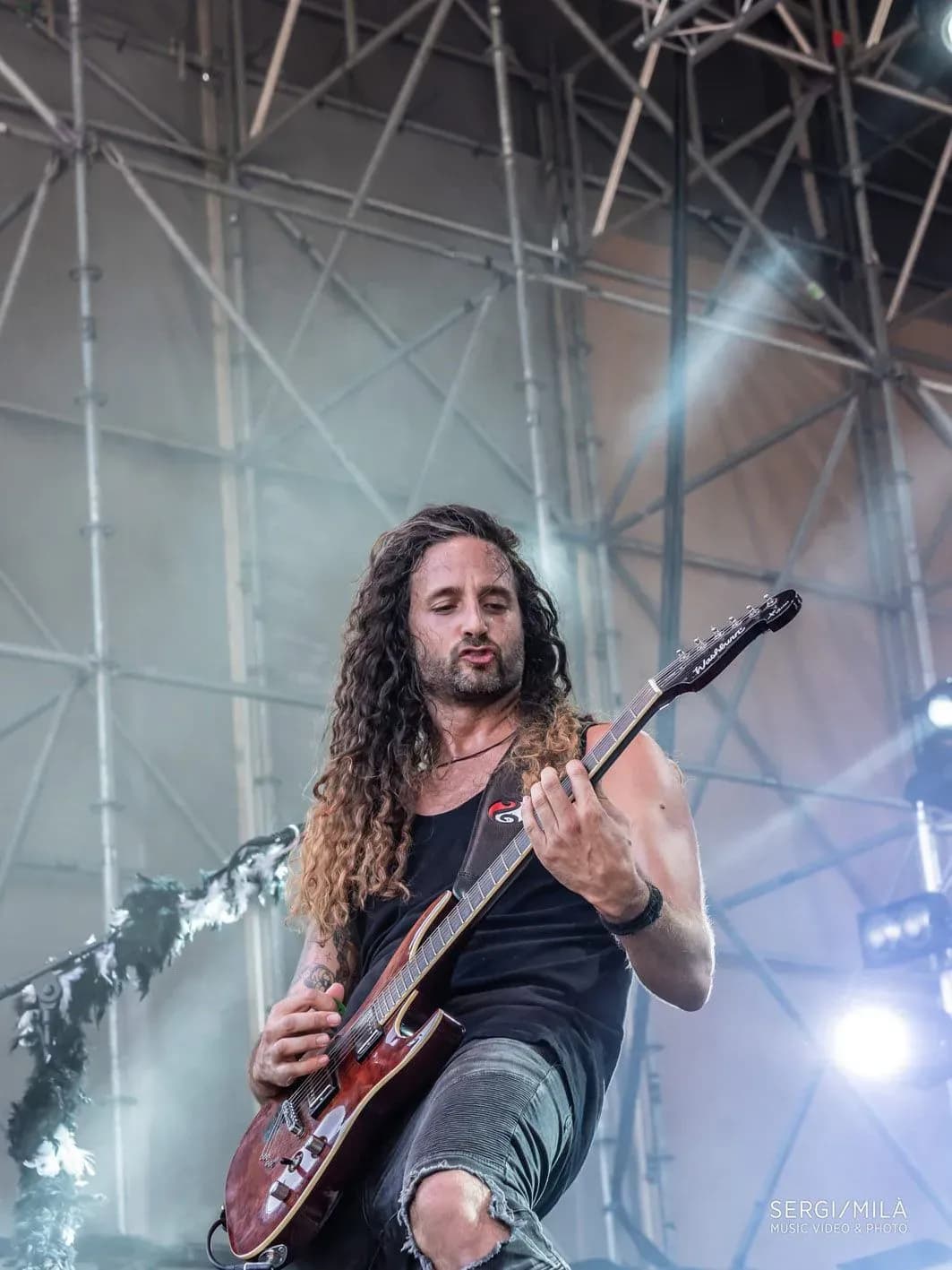 Guitarrista de Big Mouthers con melena larga y guitarra electrica roja tocando bajo estructura de festival al aire libre