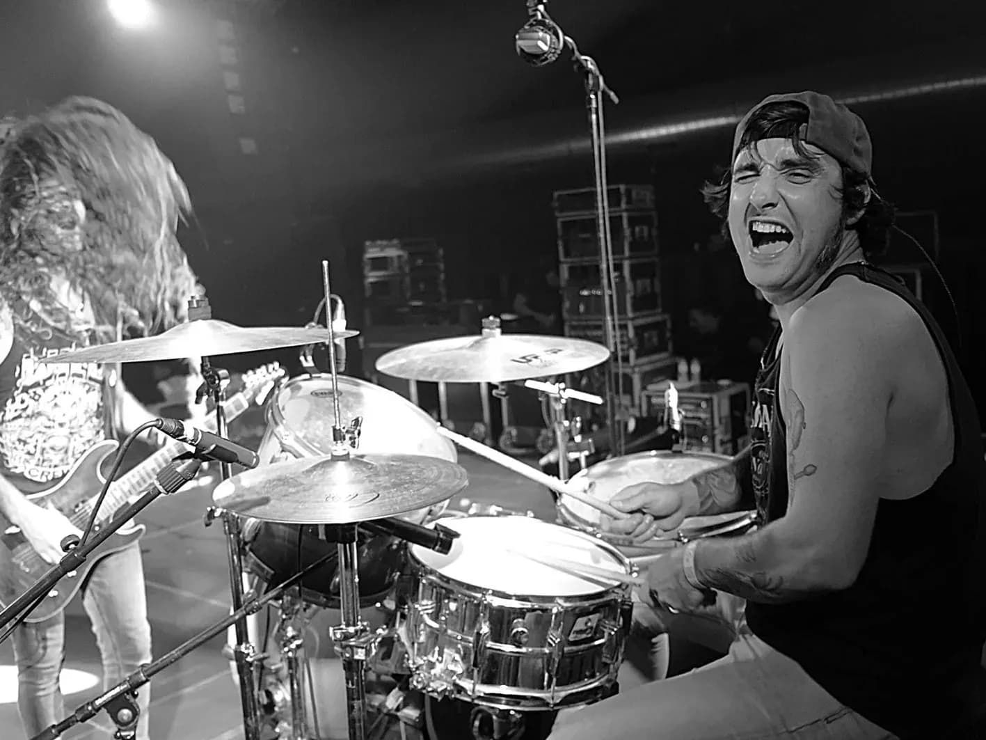Bateria de Big Mouthers gritando con gorra del reves mientras toca en directo en blanco y negro