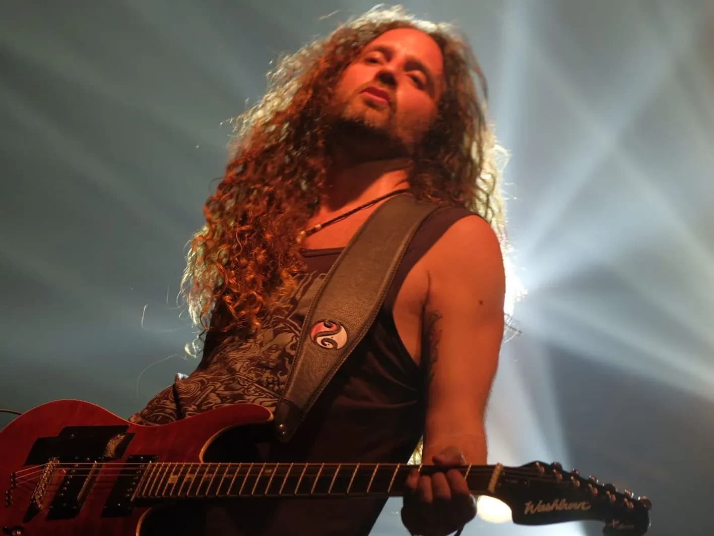 Guitarrista de Big Mouthers con melena rizada y camiseta de tirantes tocando una Washburn roja bajo focos de concierto