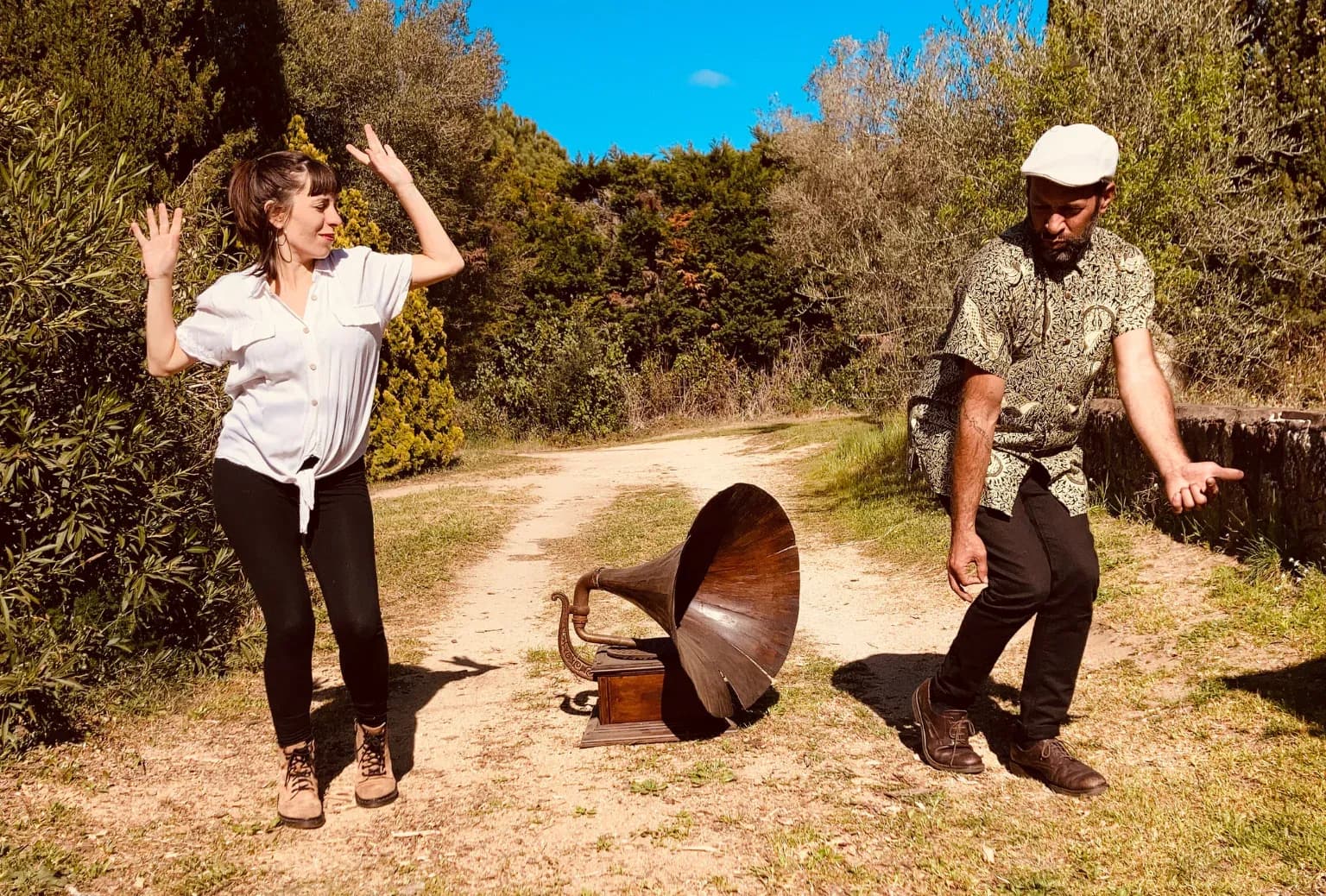 Canela N' Drama bailando junto a gramófono antiguo en camino rural soleado, fusión de voz, cajón flamenco y guitarra
