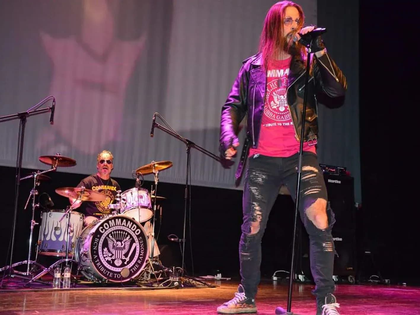 Guitarrista de Commando con flequillo Joey Ramone y chupa de cuero marrón tocando guitarra eléctrica en concierto tributo