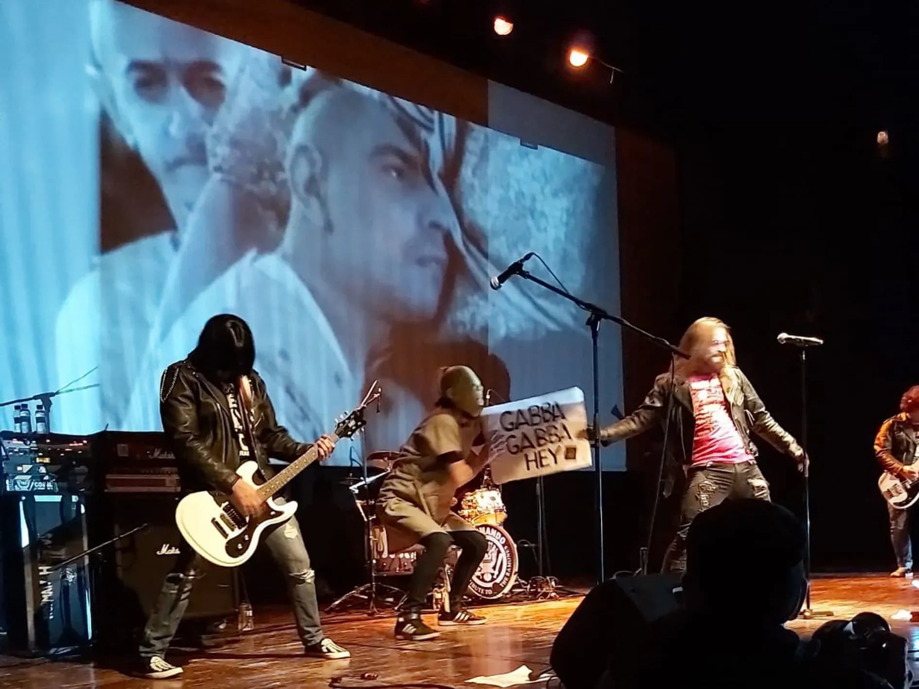 Banda Commando tributo Ramones en escenario con guitarrista, cartel Gabba Gabba Hey y proyeccion de fondo