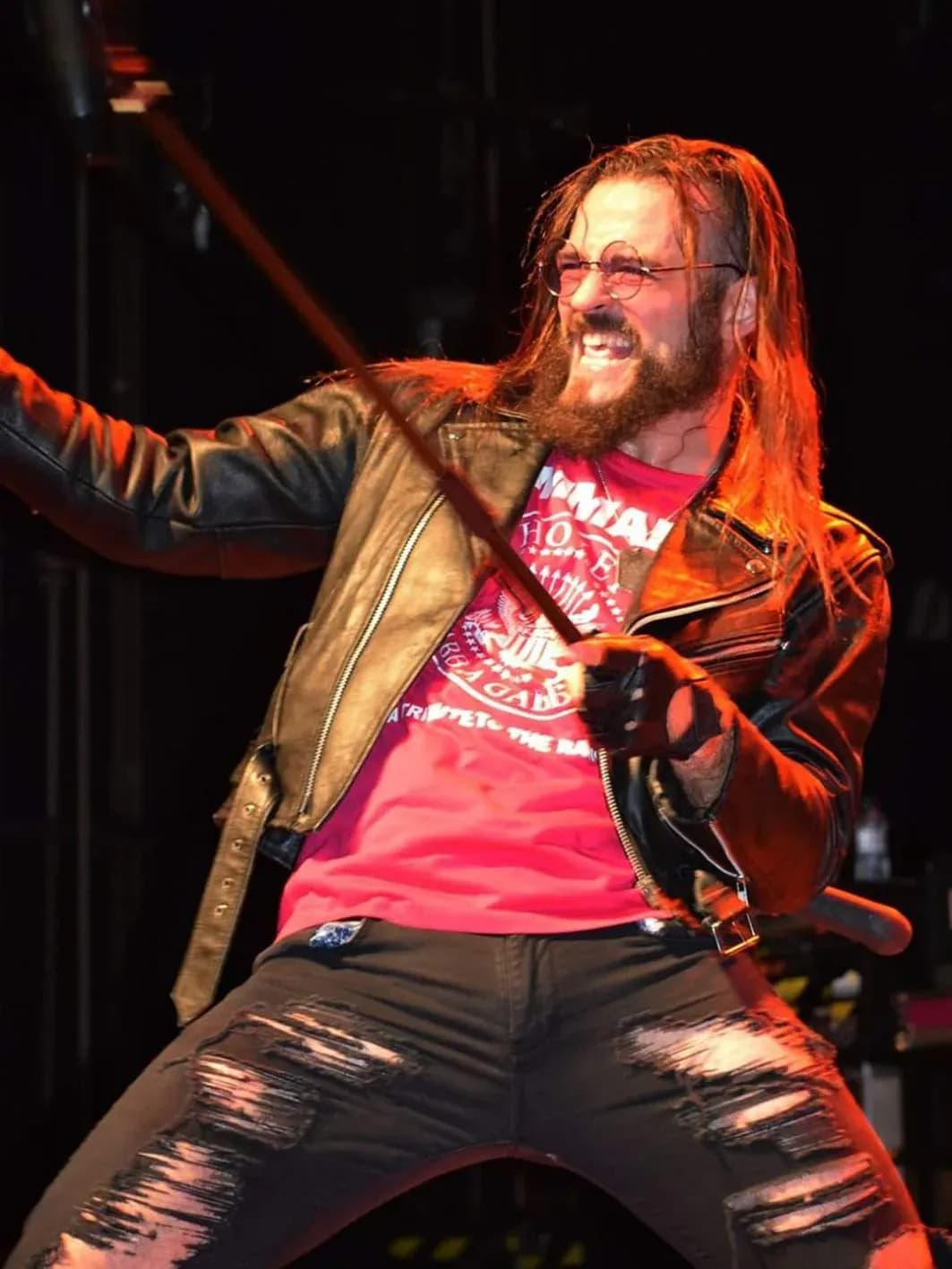 Cantante de Commando con melena pelirroja, chaqueta de cuero y micrófono en pie de pose abierta sobre escenario
