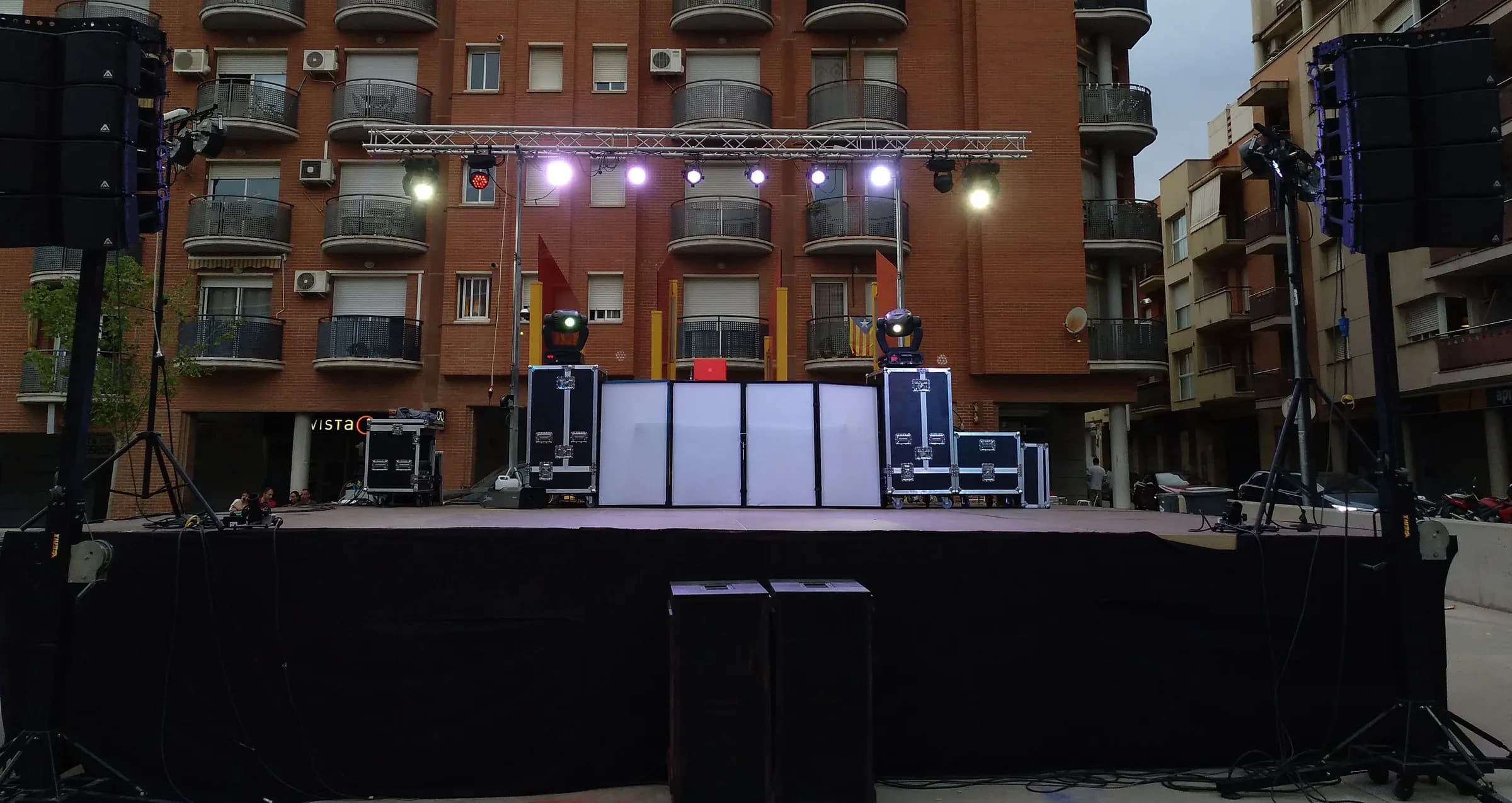 Discomovil montada en calle con escenario, line array de altavoces, focos y truss frente a edificio de viviendas