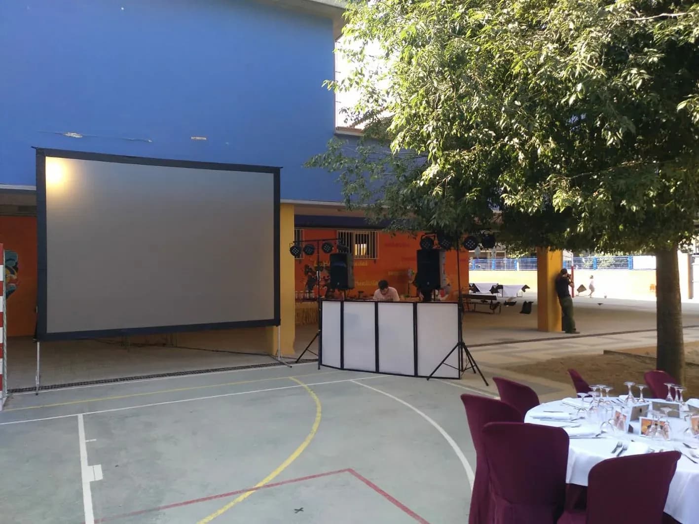 Discomovil montada en patio escolar con pantalla de proyeccion, altavoces y cabina junto a mesa preparada