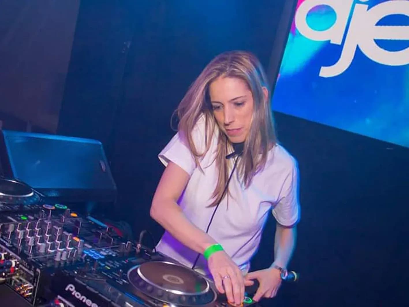 DJ Enka con camiseta blanca manipulando CDJ Pioneer ante cartel iluminado en la cabina de Disco Vipés Calafell