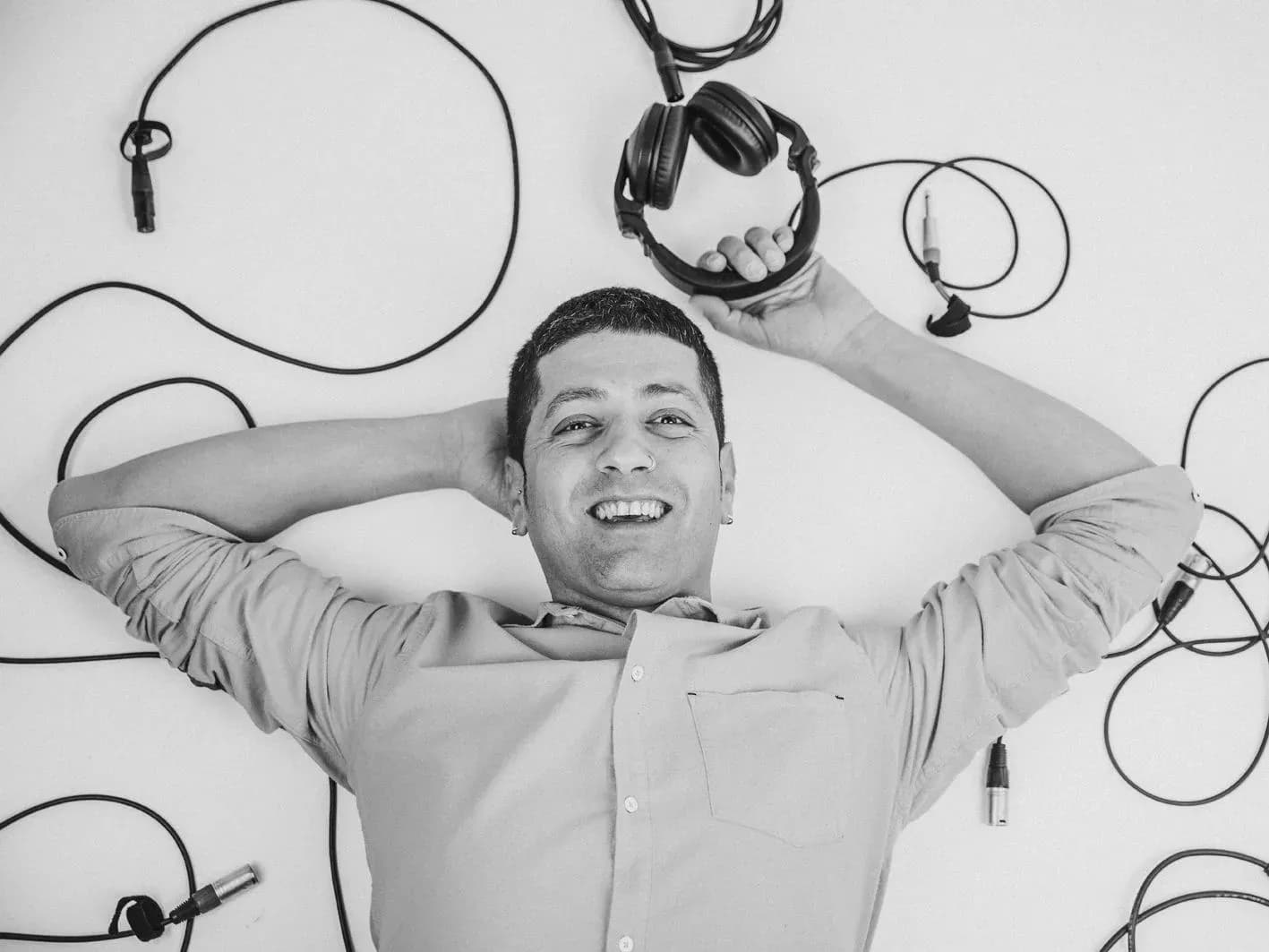 Pablo Picón tumbado entre cables XLR y auriculares en suelo blanco, retrato cenital en blanco y negro del DJ y speaker