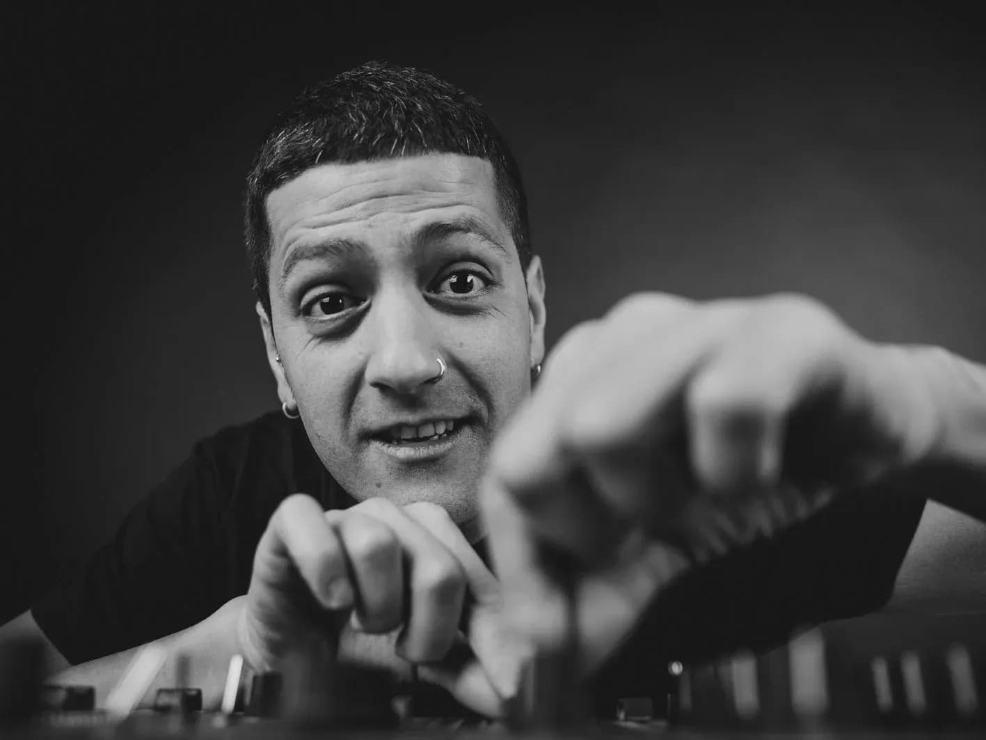 Retrato en blanco y negro de DJ Pablo mirando a camara mientras manipula faders de mesa de mezclas