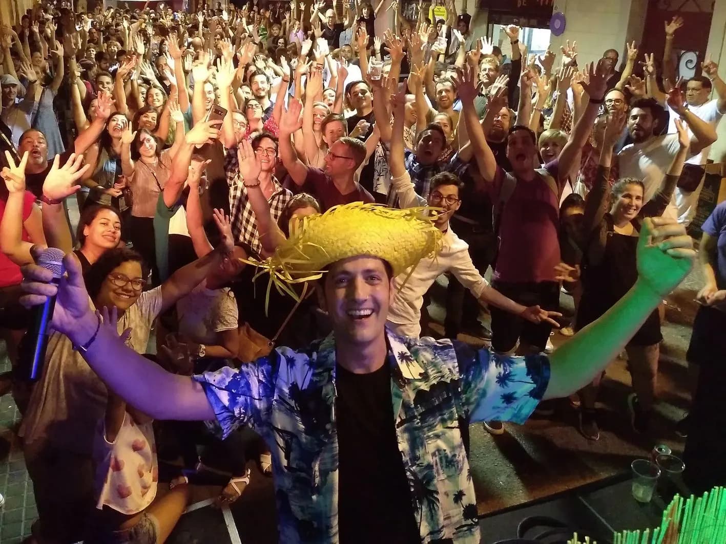 DJ Pablo con sombrero de paja y camisa hawaiana brindando con publico que alza los brazos en fiesta nocturna