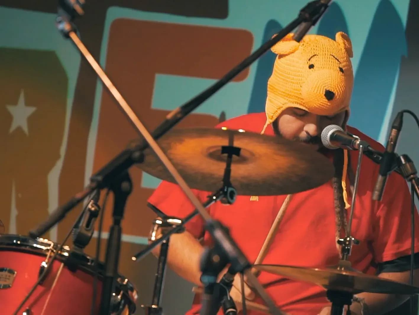 Batería de Els Kremats con gorro de ganchillo de Winnie the Pooh cantando frente al micrófono detrás de la batería