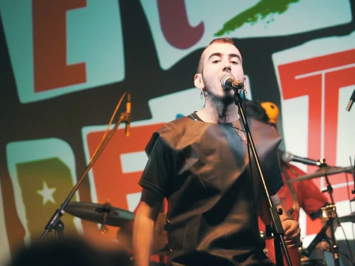 Vocalista de Els Kremats con camiseta negra de cuero cantando al micrófono ante proyección con el logo de la banda
