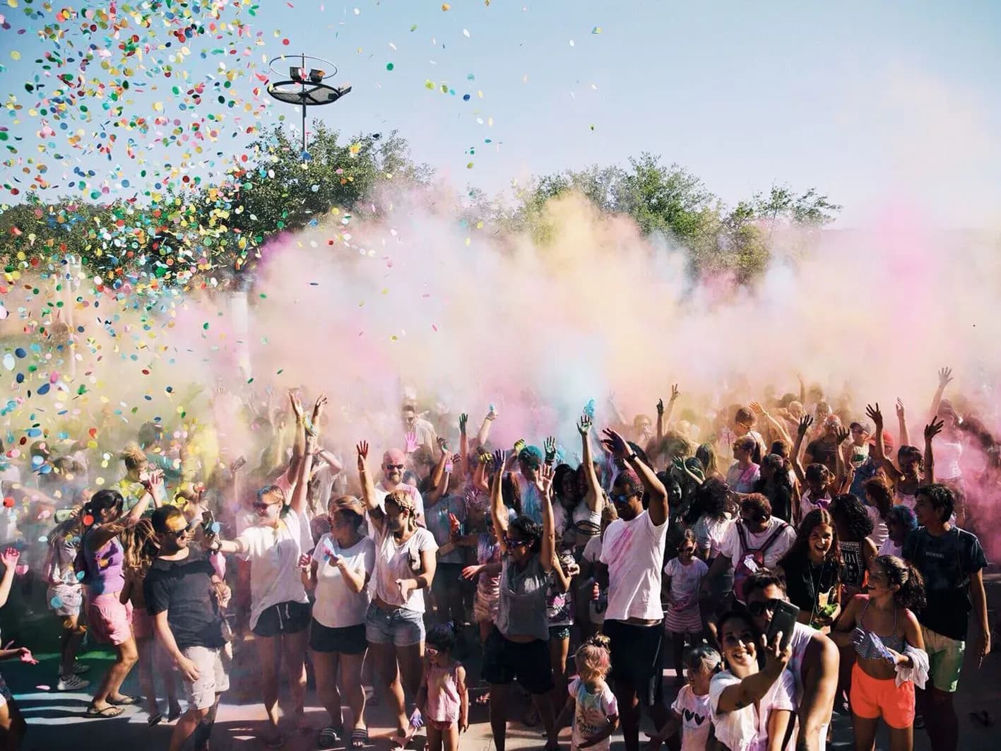 Fiesta Holi al aire libre con publico lanzando polvos de colores y confeti bajo cielo despejado
