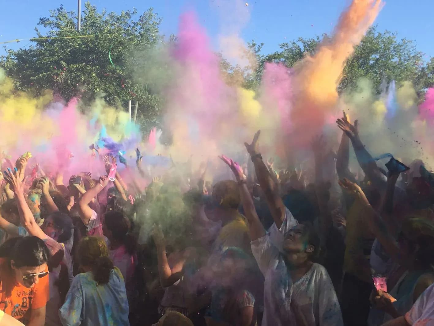 Publico con brazos en alto lanzando polvos de colores al aire en fiesta Holi al sol
