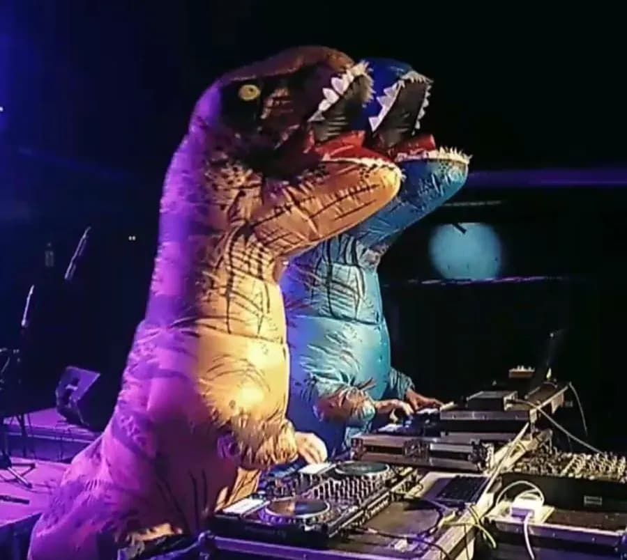 Dos DJs de Hunder Button disfrazados de T-Rex inflables pinchando en cabina con platos y mesa de mezclas