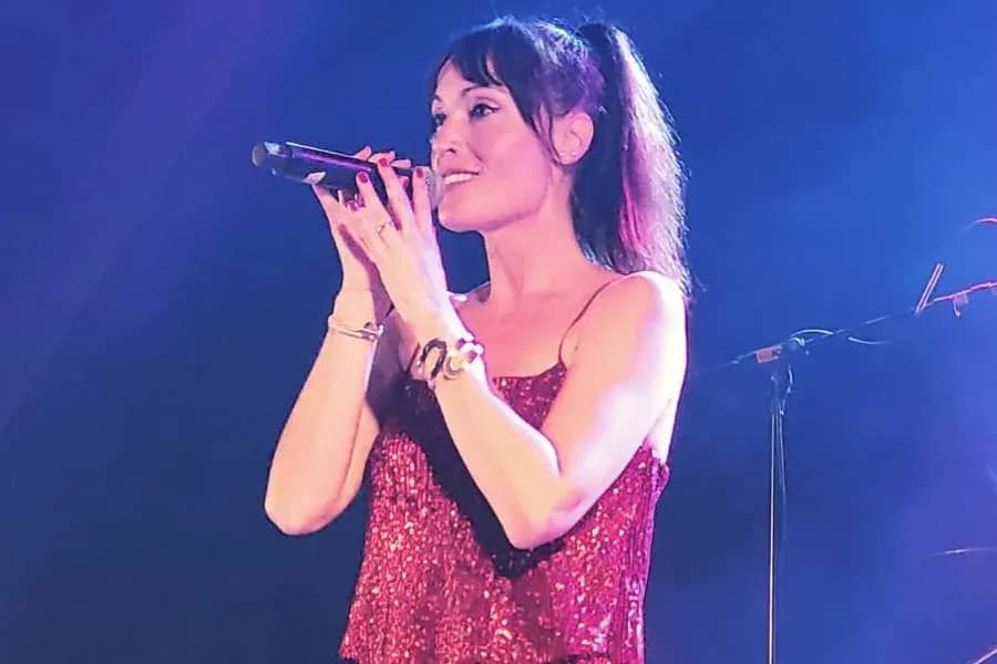 Míriam Hernández cantando con top rojo brillante y micrófono en mano sobre escenario iluminado de azul, proyecto Miris Way