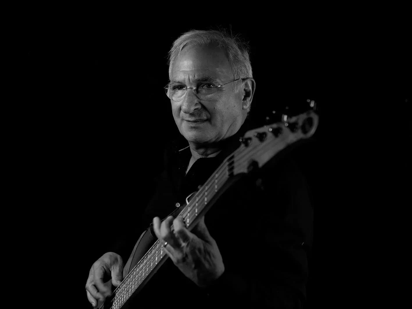 Bajista de Movie Band con gafas y bajo eléctrico de cinco cuerdas en retrato en blanco y negro sobre fondo oscuro
