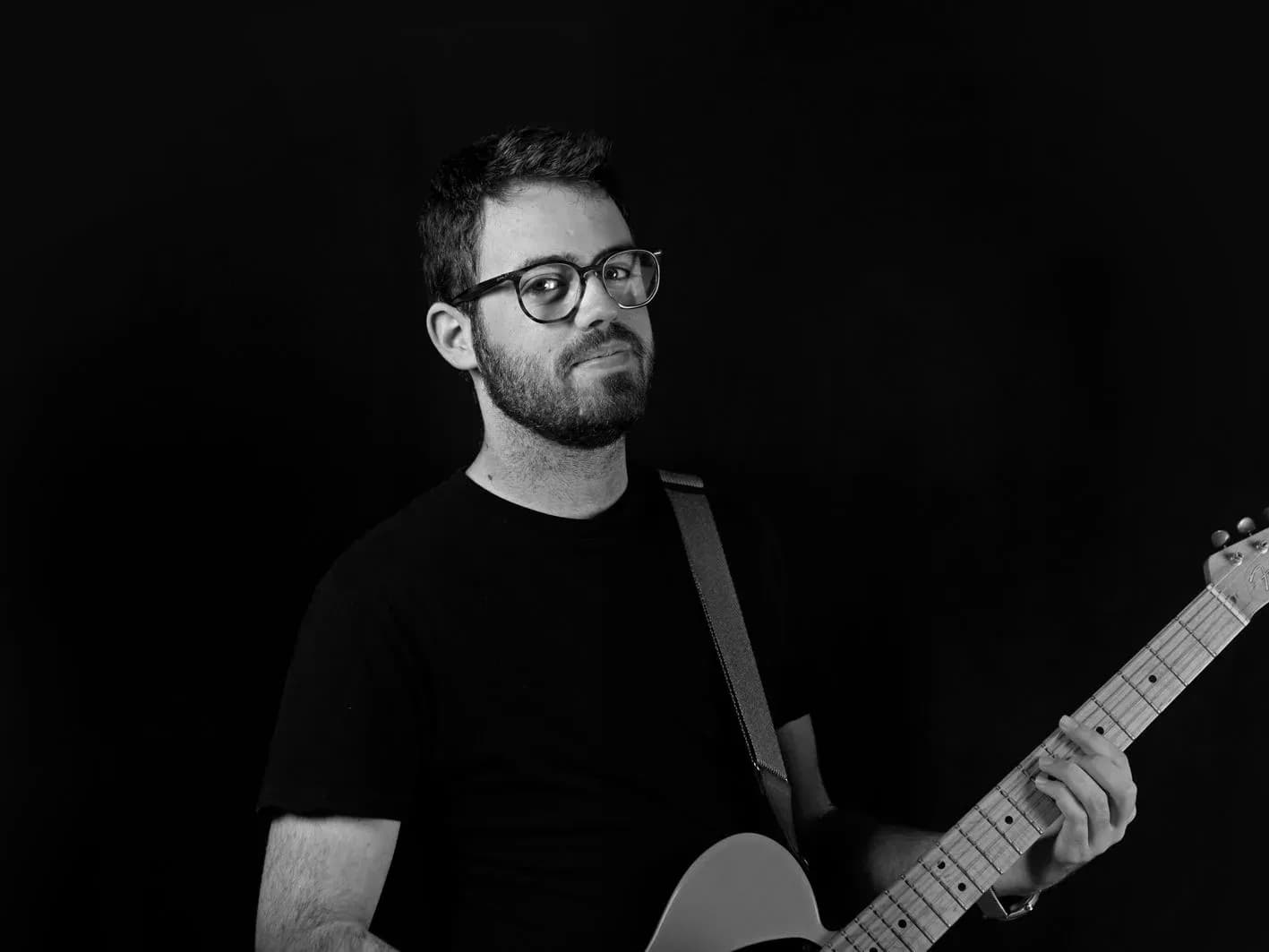 Guitarrista de Movie Band con gafas y guitarra Telecaster en retrato de estudio en blanco y negro sobre fondo negro