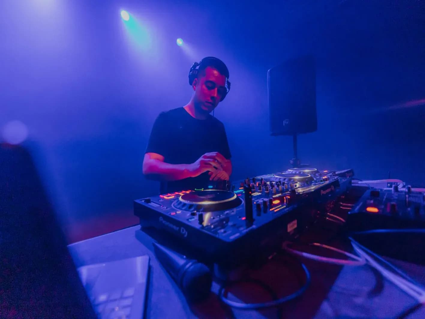 Quim Martínez con auriculares y camiseta negra entre humo azul manejando dos CDJs Pioneer en cabina de festival