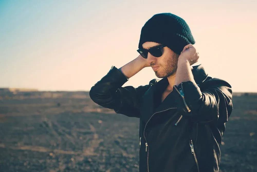 DJ de Resonance con gorro de lana y gafas de sol al atardecer en exterior con cazadora de cuero negra