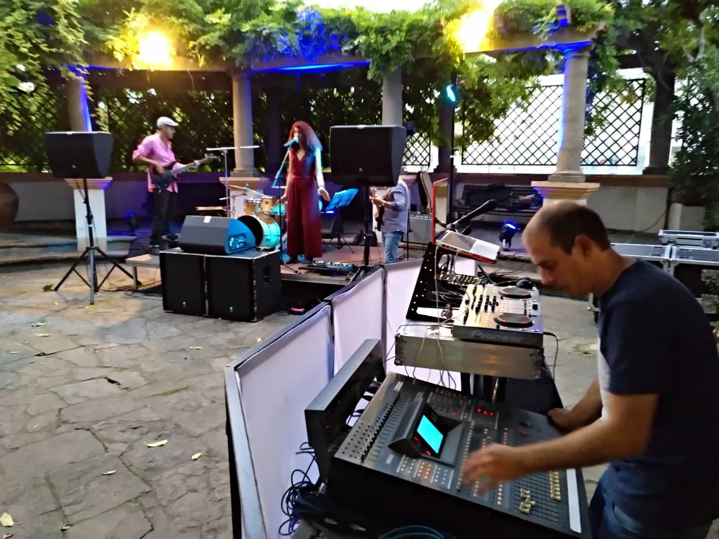 Tecnico de sonido operando la mesa de mezclas en evento al aire libre con banda tocando al fondo