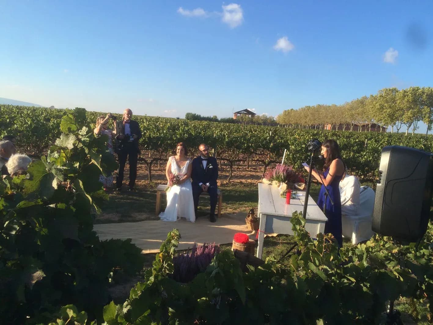 Ceremonia de boda civil al aire libre entre vinedos con los novios sentados y oficiante leyendo