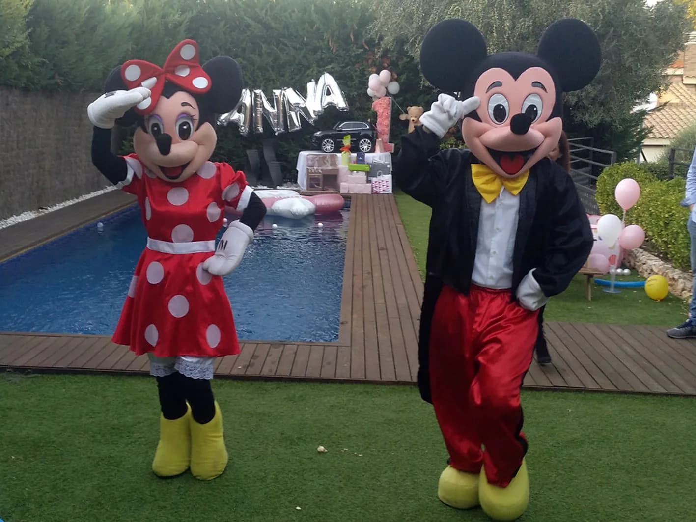Personajes disfrazados de Mickey y Minnie posando junto a piscina con globos plateados ANNA en fiesta de cumpleaños